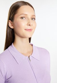 Top a coste lilla con colletto e zipper corta. Presenta un design aderente e una texture liscia, evidenziando un'estetica pulita e moderna.