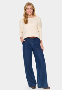 Kreemised pika varrukaga särk laia kaelusega, millele on lisatud tumedast sinisest laiade säärega teksad. Riietust täiendavad pruun vöö ja saapad.