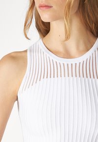 Vit ribbad linne med genomskinlig randig detalj vid halsringningen och axeln. Slät textur med en figurnära design.