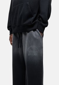 Zwarte hoodie met voorzak, gecombineerd met grijsachtige sweatpants met een gradient, voorzien van tekst en een vlindergrafiek op de rechterdij.