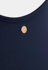Tengerészeti fürdőruha anyag, kerek nyakkivágással, lapos varrással, és egy kis aranyozott fém díszítéssel, amelyen a "MINT" felirat található.