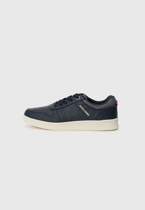 Navy sneaker with textured leather and a white sole. Features laces and logo detailing on the side. Neutral background accentuates design.