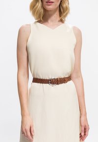 Kremowa sukienka bez rękawów z dekoltem w kształcie litery V oraz teksturowanym, plecionym brązowym paskiem z okrągłą metalową klamrą. Gładka tkanina z delikatnym układaniem.
