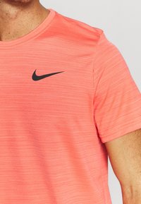 Camiseta deportiva de manga corta y cuello redondo en tejido coral jaspeado, con un logotipo negro de Nike en la parte superior izquierda del pecho.