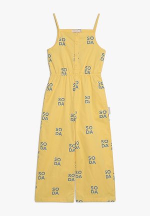Żółty kombinezon na regulowanych cienkich ramiączkach, zapinany na guziki z przodu, z elastyczną talią oraz powtarzającym się niebieskim wzorem "SODA" na całej powierzchni.