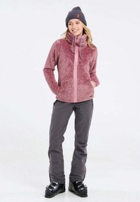 Giacca in pile maroon, morbida e di peso medio, con colletto alto e zip rosa; abbinata a pantaloni grigi e stivali da neve neri. Inclusa un berretto.