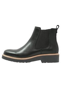 Stivale Chelsea in pelle nera con pannello laterale elasticizzato, cuciture color cuoio, linguetta sul tallone e suola in gomma spessa con tacco basso.