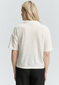 Valge lühikeste varrukatega polo särk tekstuuriga kangast. Igapäevane disain krae ja vaba lõikega, koos mustade pükstega.