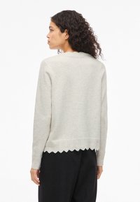 Suéter bege claro com bainha ondulada e detalhe intricado em tricô. Apresenta mangas compridas e decote redondo. Textura macia.