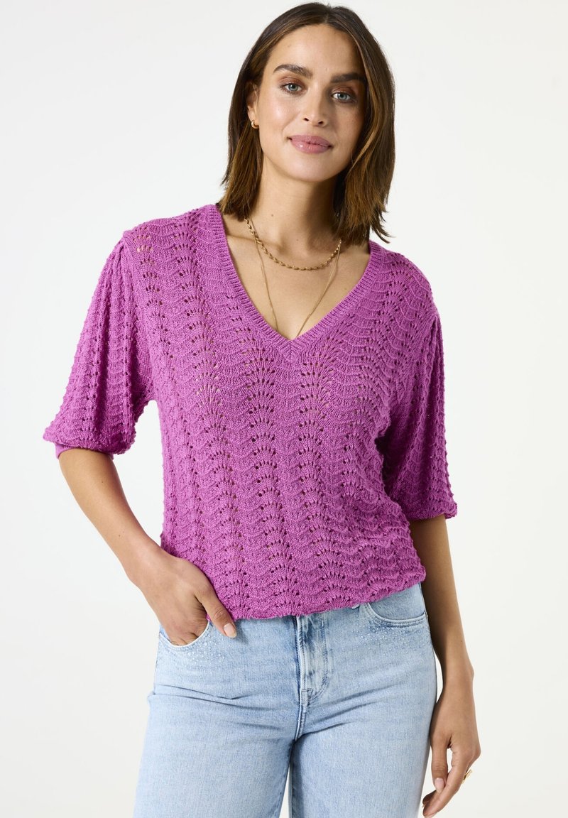 Gehaakte top in felle roze met een V-hals, korte mouwen en een textuurpatroon, gecombineerd met lichtblauwe spijkerbroeken.