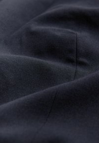 Gros plan sur un tissu lisse de couleur bleu marine foncé avec de douces plis et des coutures visibles créant des courbes douces.