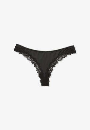 Tanga de encaje negro con ribete de encaje floral a lo largo de los bordes y cuerpo suave con acabado satinado. Presenta un diseño de tiro bajo y cobertura mínima en la parte trasera.