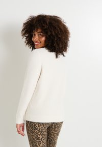 Suéter de color crema, de textura suave, con un escote redondeado y mangas largas; combinado con pantalones de leopardo marrón.