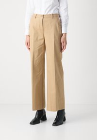Trousers in beige cotton, wide-leg design, featuring a front button closure and side pockets, paired with black heeled ankle boots.