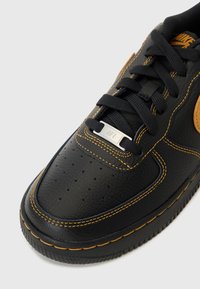 Must musta sneaker, millel on teksuuriga viimistlus, kollased õmblused ja pruunist nahast aktsent. Sisaldab perforatsiooni varbaosas ja metallist logo detaili.