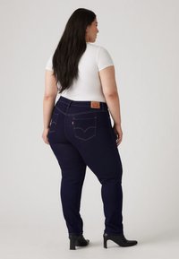 Mörkblå jeans med en figurnära design, med bakfickor och en märkeslädermärke vid midjebandet. Kombinerade med en vit skjorta och svarta klackar.