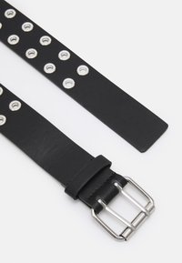 Cinto de couro preto com ilhós metálicos de um lado, apresentando uma fivela prateada e textura lisa. As extremidades são cortadas em linha reta.