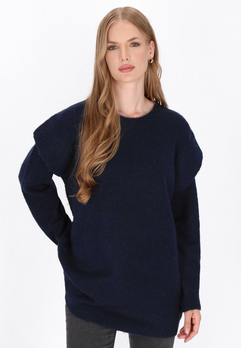Granatowy sweter dzianinowy z długimi rękawami, opadającymi szwami na ramionach i ściągaczami przy mankietach. Miękka tekstura, luźny krój oraz okrągły dekolt.