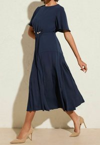 Námořnické midi šaty s krátkými rukávy a detailem zavázaného pasu, s volánkovou sukní a hladkým materiálem. V kombinaci s nahými lodičkami.