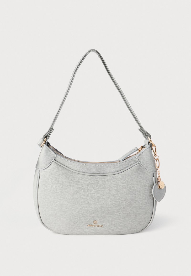 Grijze leren handtas met een gebogen vorm, hardware in goudkleur en een decoratieve hanger. Voorzien van een ritssluiting en een enkele schouderriem.