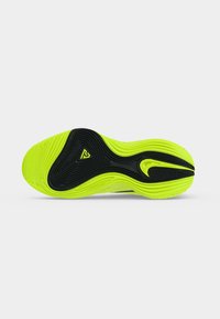 Semelle de chaussure de sport jaune vif et noire avec des rainures texturées et le logo Nike, vue de dessous sur fond blanc.