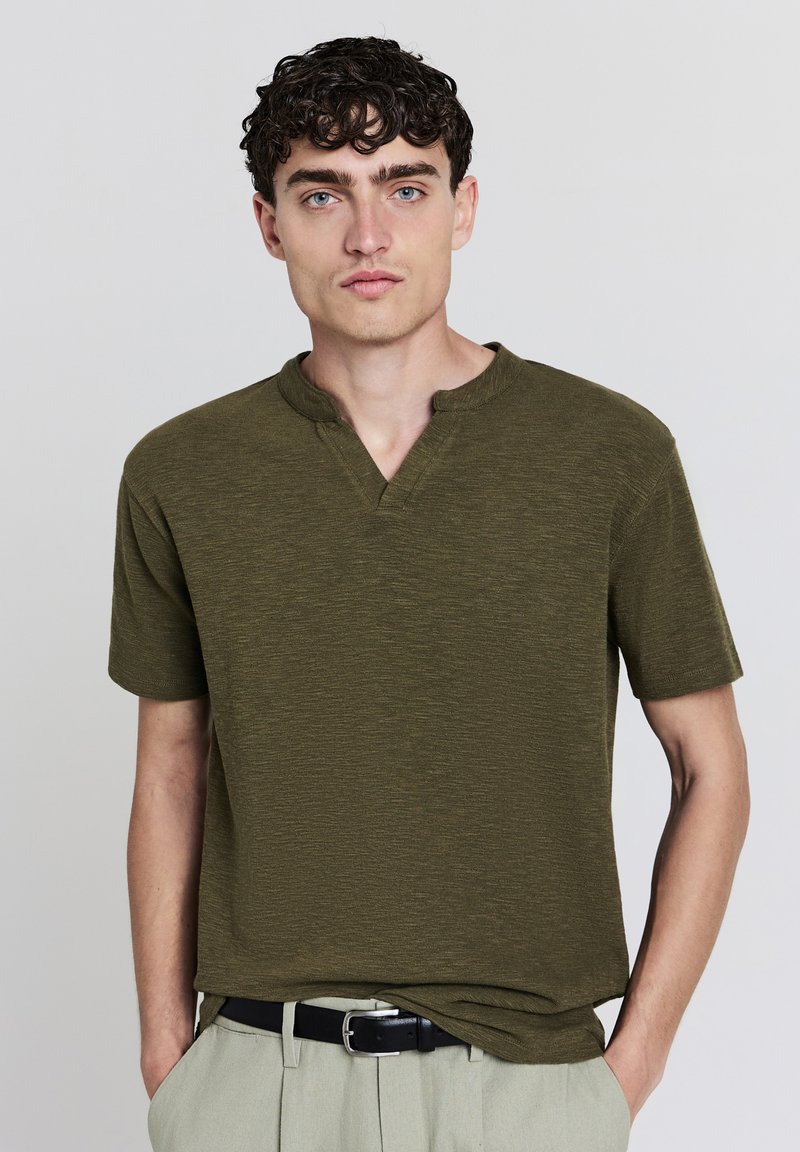 T-shirt verde oliva a maniche corte con un tessuto testurizzato, caratterizzato da un collo rotondo e una vestibilità rilassata. Superficie liscia con leggere variazioni.