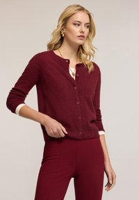 Burgundské kardigan z měkkého materiálu s texturovaným povrchem, s kulatým výstřihem, zapínáním na knoflíky a dlouhými rukávy s bílými manžetami.