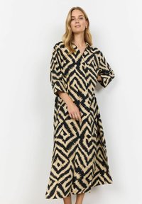 Midi shirtjurk in zwart en beige, met een zigzagpatroon, een kraag en brede mouwen. Gemaakt van een lichte stof met een vloeiende silhouet.