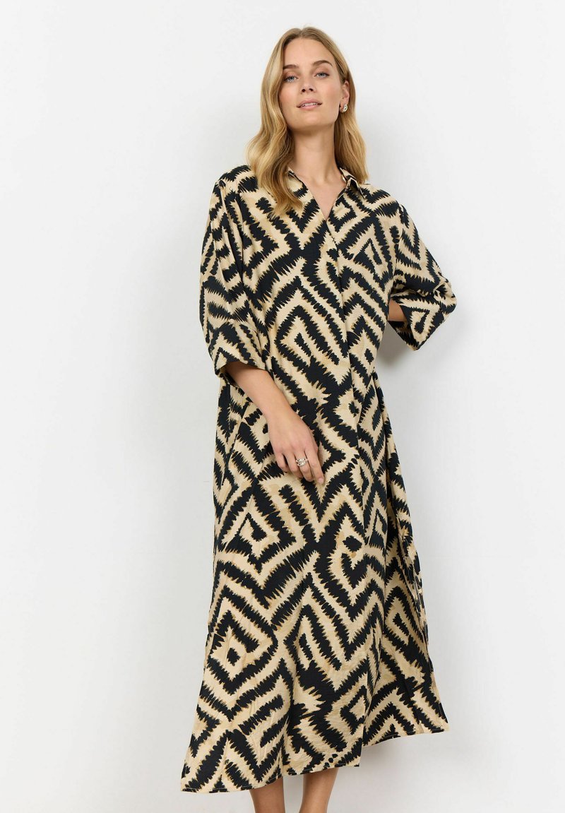 Midi shirtjurk in zwart en beige, met een zigzagpatroon, een kraag en brede mouwen. Gemaakt van een lichte stof met een vloeiende silhouet.