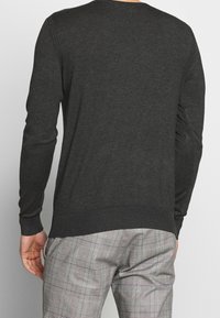 Dark gray sweater with a round neckline, long sleeves, and ribbed cuffs; smooth texture, fitted shape. Worn with checkered gray pants.
