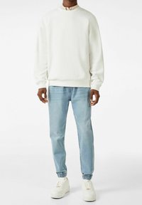 White sweatshirt with a rounded neckline, relaxed fit, and ribbed cuffs, paired with light blue tapered jeans and white sneakers.