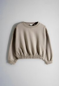 Taupekleurige cropped sweatshirt met lange mouwen en een elastische tailleband en manchetten, plat neergelegd tegen een lichtgrijze achtergrond.