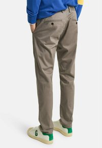 Pantalones caqui de corte estándar, con dos bolsillos traseros y una textura de tela suave, combinados con zapatillas blancas con acentos verdes.