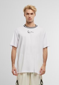 Hvid kortærmet T-shirt med en sort stribet rund hals og en minimalistisk sort signaturgrafik på brystet. Letvægtsstof.