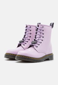 Jasnofioletowe botki do kostki o błyszczącej powierzchni, czarne sznurowanie, kontrastowe żółte szwy oraz fakturowana czarna gumowa podeszwa.