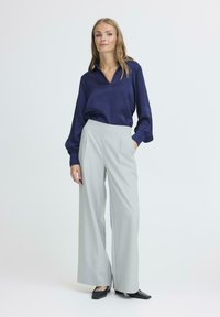 Tamsiai mėlyna satino ilgos rankovės bluzonė su V formos iškirpte, derinama su šviesiai pilkais plačiais kelnais. Juodi smailiagalviai balerinos bateliai užbaigia aprangą.