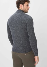 Dunkelgrauer Strickpullover mit Stehkragen, strukturiertem Muster und tailliertem Schnitt. Getragen mit olivgrünen Hosen.
