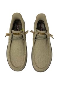 Zapatos deslizables beige con superior de tela texturizada, cordones flexibles y plantilla acolchada. Presenta detalles de marca acentuados en la lengüeta.