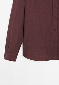 Burgundská košile s dlouhým rukávem na knoflíky z mírně texturované tkaniny, s oblým lemem a standardními manžetami. Šest odpovídajících knoflíků je viditelných.
