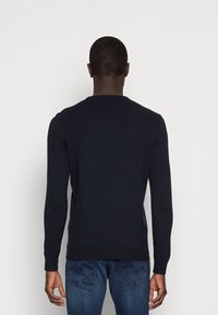 Maglione blu scuro a girocollo con maniche lunghe, polsini e orlo a costine, mostrato da dietro su uno sfondo bianco semplice.