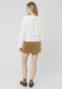 Blouse blanche avec broderies florales et détails en jour échelle. Jupe en velours côtelé marron. Associée à des chaussures marron et des chaussettes à motifs. Vue arrière.