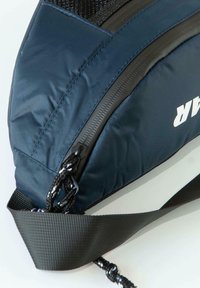 Navy nylon bag with a textured black mesh panel, featuring a prominent zipper, a durable strap, and a white logo on the side.