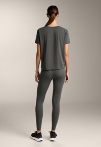 Harmaa puuvillainen t-paita rentoa fit'iä, yhdistettynä harmaisiin joustaviin legginsseihin. Jalkineet ovat mustat urheilukengät, joissa on valkoiset pohjat.