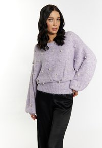 Pulover oversized lila cu embellishments de perle, tiv cu striații și mâneci lungi, asortat cu pantaloni negri din satin. Material moale, texturat.