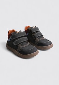 Zapatos negros con correas de Velcro, que cuentan con suelas de goma marrón, superposición texturizada y acentos coloridos en la lengua y el talón.
