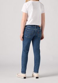 Blå denimjeans med slim fit, med medelhögt midjeband, bakfickor med sömnadsdetaljer, i kombination med en vit t-shirt med kort ärm.