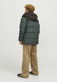 Pufferjack met een capuchon in donker teal en zwart, met een gequilt textuur. Gecombineerd met beige wijde pantalons en zwarte schoenen.