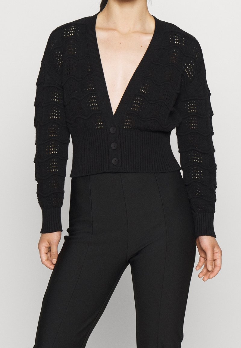 Czarny cropped kardigan z głębokim dekoltem w V, z wzorem falistym oraz poziomymi prążkami, z zapięciem na guziki i dopasowanymi rękawami.