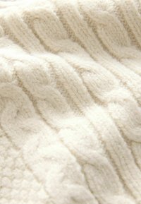 Couverture en laine tricotée à câble de couleur blanc cassé, avec des nervures texturées et une surface douce et pelucheuse pour la chaleur et le confort.
