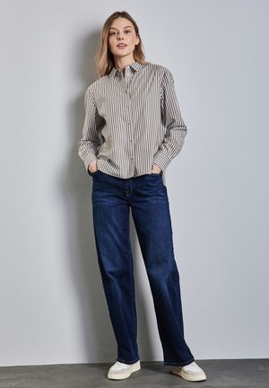 Camicia a maniche lunghe con colletto, a righe verticali beige e marrone scuro, abbinata a jeans dritti blu scuro e sneakers bianche.